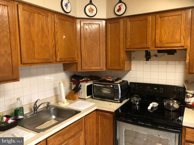 kitchen featuring brown cabinets, a toaster, range with electric stovetop, light countertops, and a sink