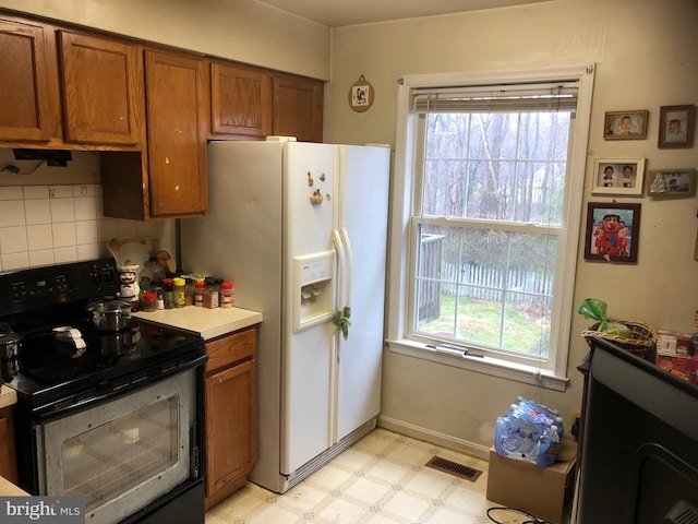 kitchen with light floors, visible vents, brown cabinetry, white fridge with ice dispenser, and stainless steel electric range