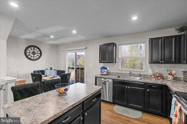 kitchen with a sink, appliances with stainless steel finishes, dark cabinetry, and light wood finished floors