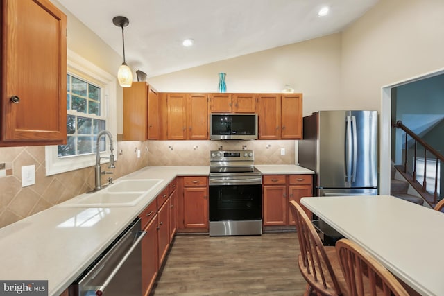 kitchen featuring lofted ceiling, a sink, hanging light fixtures, light countertops, and stainless steel appliances