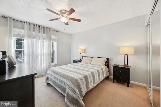 bedroom with a ceiling fan, light colored carpet, baseboards, and a textured ceiling