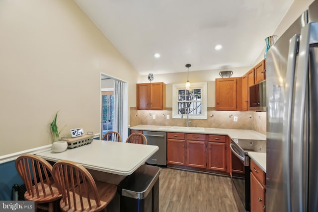 kitchen with a kitchen bar, stainless steel appliances, a peninsula, light countertops, and vaulted ceiling