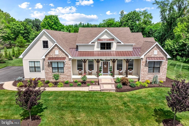 craftsman-style home with brick siding, roof with shingles, a standing seam roof, a porch, and a front yard