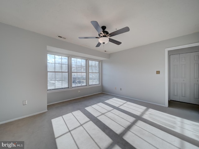 unfurnished room with ceiling fan, carpet, visible vents, and baseboards