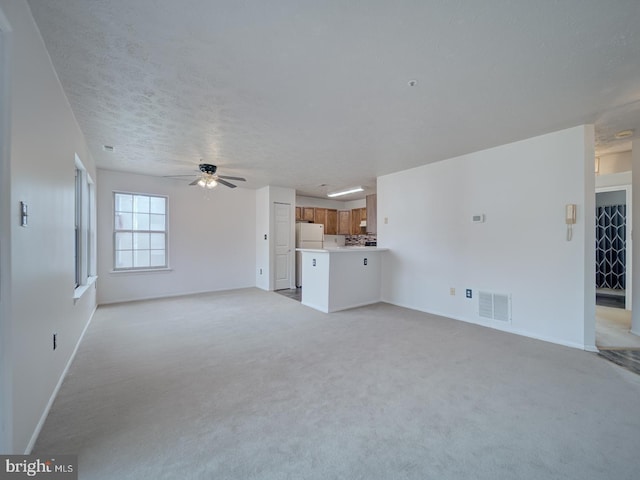 unfurnished living room featuring ceiling fan, a textured ceiling, light colored carpet, visible vents, and baseboards