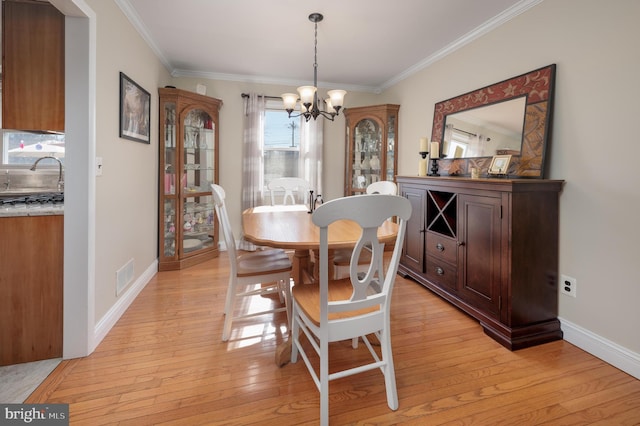 dining area featuring an inviting chandelier, light wood-style flooring, visible vents, and ornamental molding