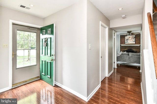 entryway featuring baseboards, visible vents, a ceiling fan, wood finished floors, and a brick fireplace