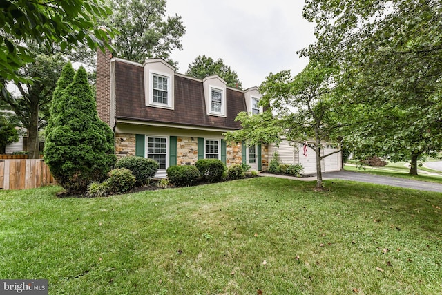 dutch colonial with driveway, stone siding, a chimney, fence, and a front lawn