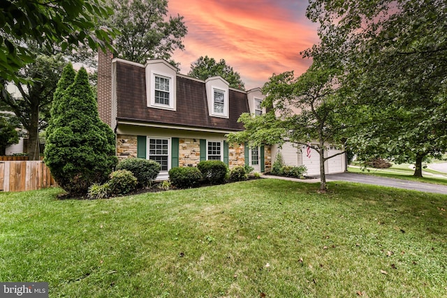 dutch colonial featuring stone siding, aphalt driveway, a front yard, and fence