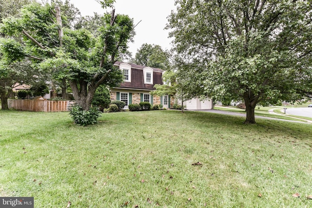 colonial inspired home with an attached garage, roof with shingles, a front yard, and fence