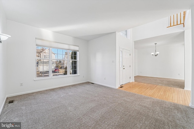 unfurnished living room with a chandelier, carpet, visible vents, and baseboards