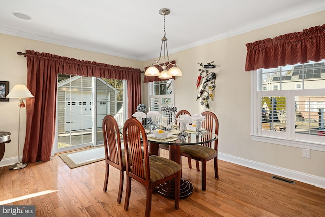 dining space featuring a chandelier, wood finished floors, visible vents, baseboards, and crown molding