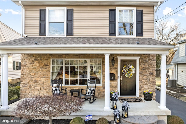 property entrance with stone siding, a porch, and roof with shingles