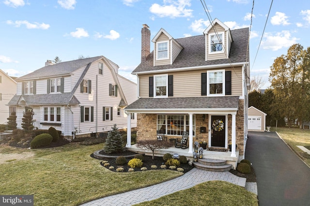 view of front of property with stone siding, roof with shingles, an outbuilding, covered porch, and a front yard