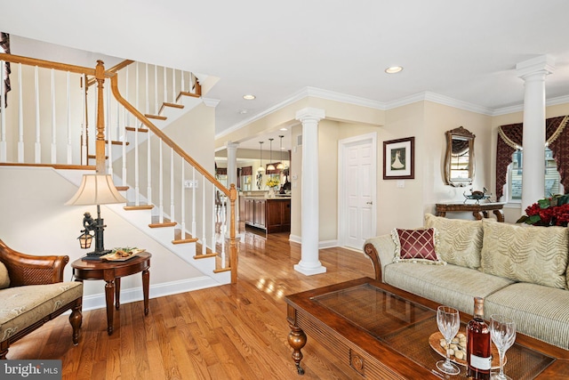 living area featuring stairs, ornamental molding, light wood-style flooring, and ornate columns