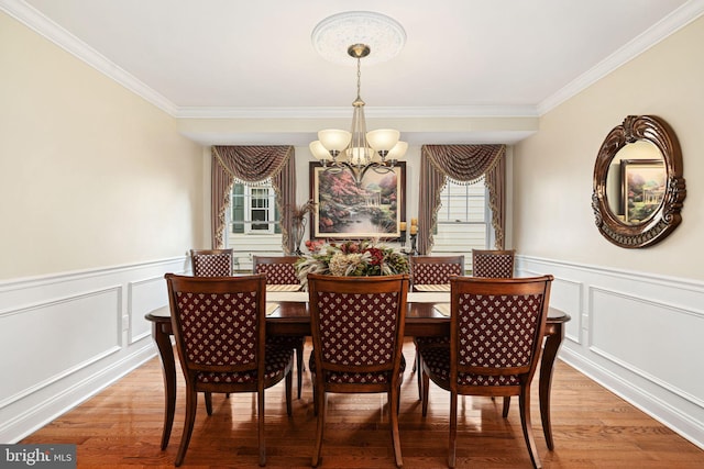 dining room with crown molding, wainscoting, light wood-style flooring, and a notable chandelier