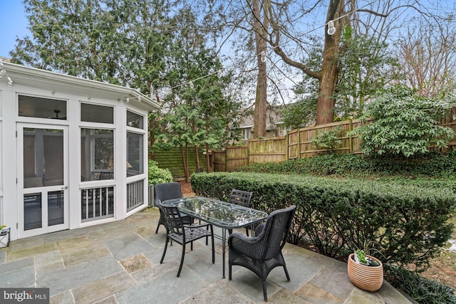 view of patio with outdoor dining area, fence, and a sunroom