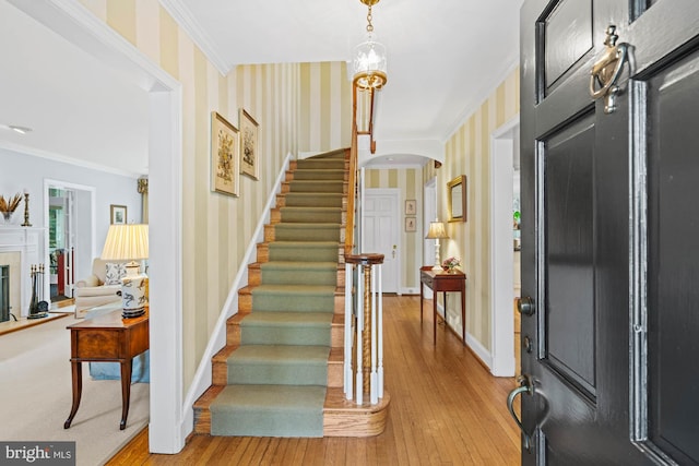 foyer featuring crown molding, baseboards, arched walkways, and wallpapered walls