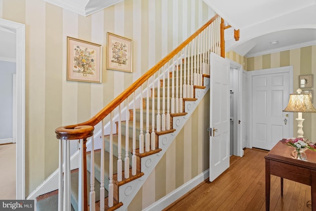 stairway featuring baseboards, hardwood / wood-style floors, crown molding, and wallpapered walls