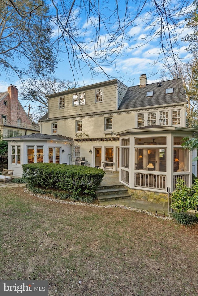 back of property featuring a sunroom, a yard, and a chimney