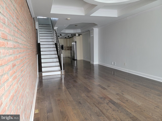 unfurnished living room with dark wood-style flooring, stairway, ornamental molding, brick wall, and baseboards