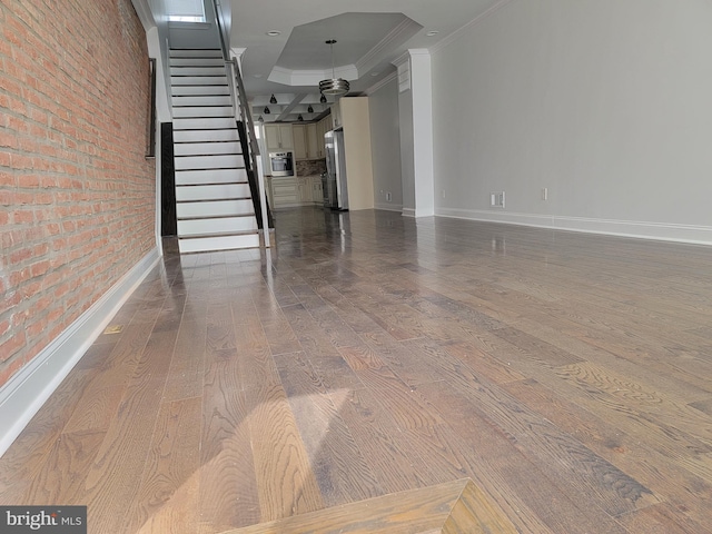 unfurnished living room with hardwood / wood-style floors, baseboards, stairs, ornamental molding, and a tray ceiling