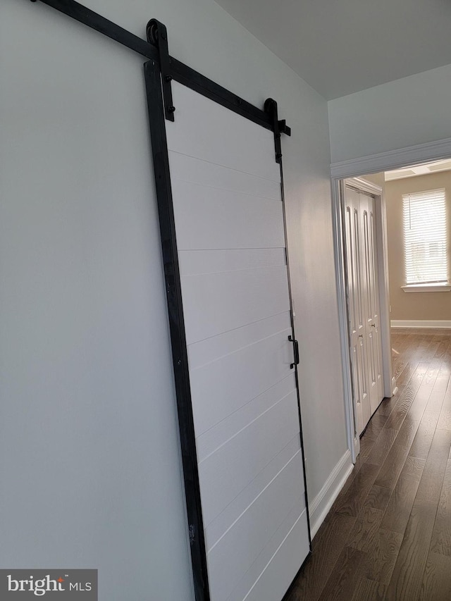 hallway with a barn door, baseboards, and dark wood-style flooring