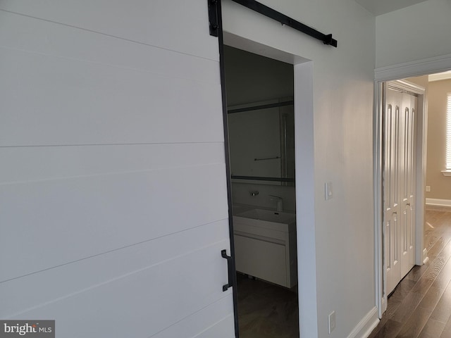 hall with dark wood-style floors, a barn door, baseboards, and a sink