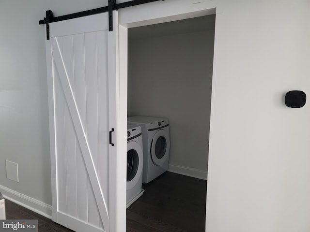 clothes washing area featuring laundry area, a barn door, baseboards, washer and clothes dryer, and dark wood finished floors