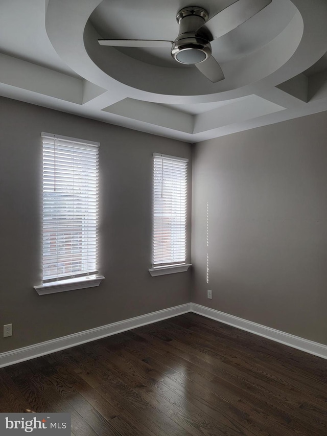 empty room with baseboards, a tray ceiling, dark wood-type flooring, and a ceiling fan