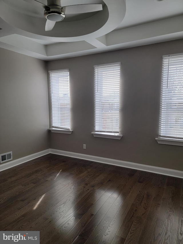 unfurnished room with ceiling fan, visible vents, dark wood-style flooring, and baseboards