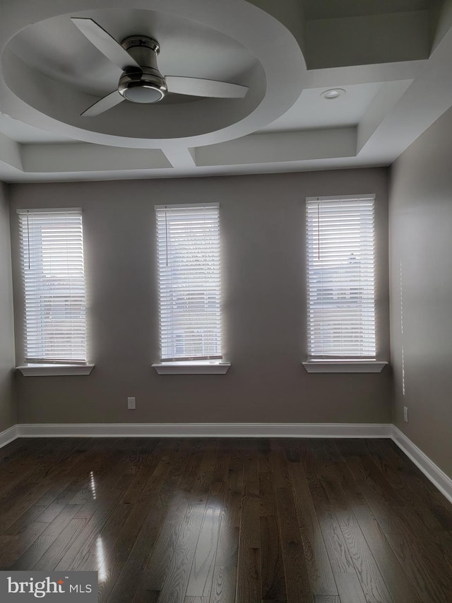 spare room featuring ceiling fan, a tray ceiling, dark wood-style flooring, and baseboards