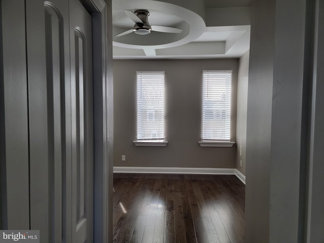 empty room with dark wood-style floors, a ceiling fan, and baseboards