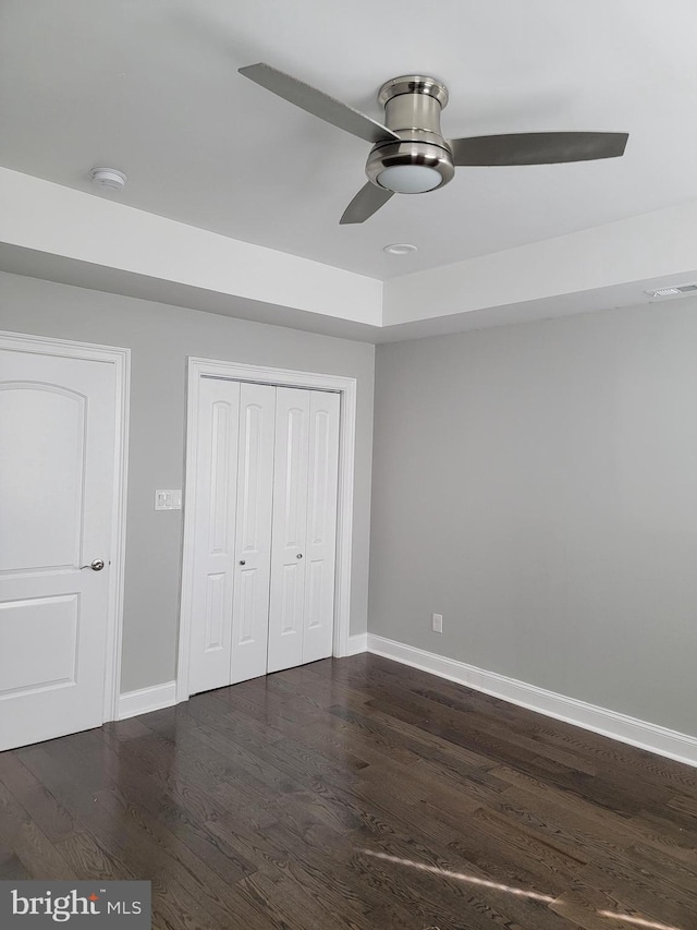 unfurnished bedroom featuring baseboards, visible vents, ceiling fan, dark wood-type flooring, and a closet