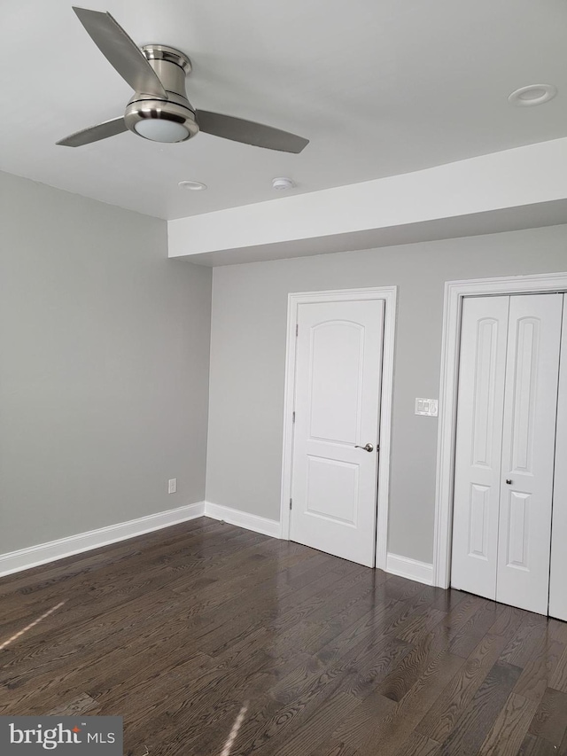 unfurnished bedroom featuring dark wood-type flooring, a closet, a ceiling fan, and baseboards