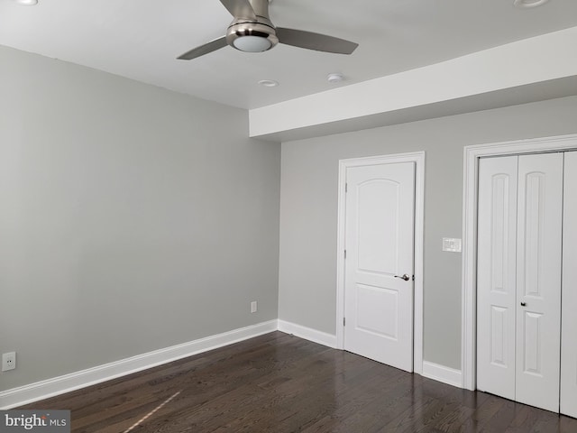 unfurnished bedroom with a closet, dark wood finished floors, baseboards, and ceiling fan