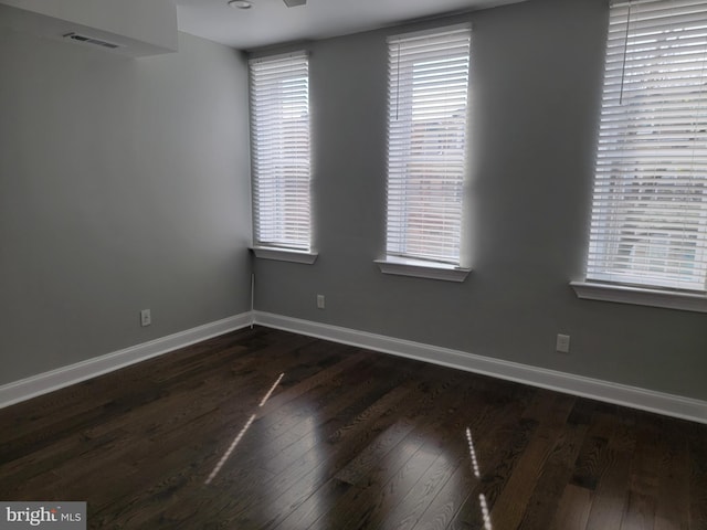 unfurnished room featuring a wealth of natural light, visible vents, baseboards, and dark wood-style flooring