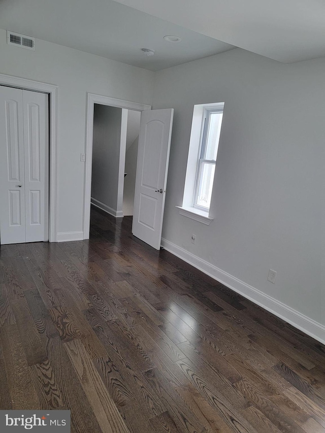 unfurnished bedroom featuring a closet, visible vents, dark wood finished floors, and baseboards