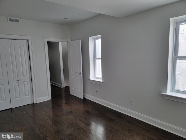 unfurnished bedroom featuring multiple windows, visible vents, and dark wood finished floors