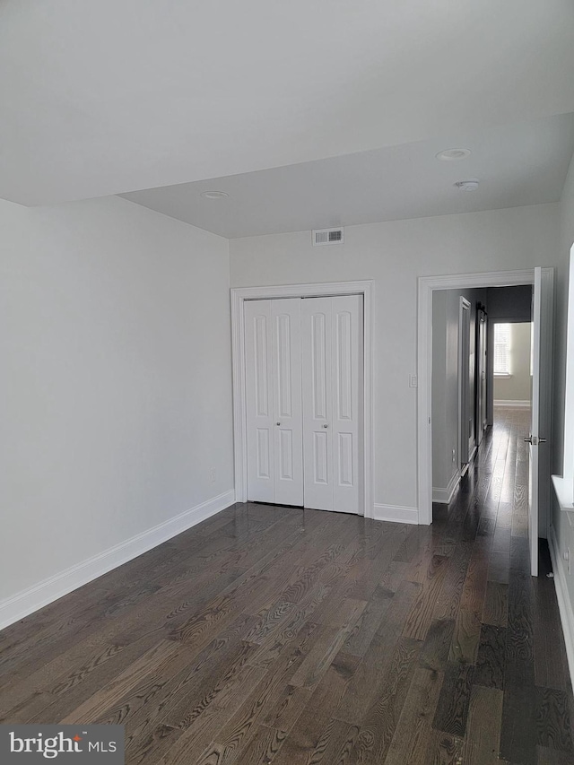 unfurnished bedroom with dark wood-style floors, visible vents, and baseboards