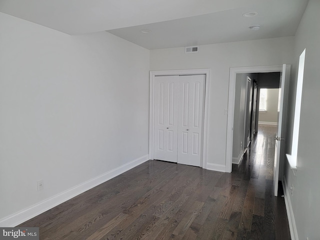 unfurnished bedroom with a closet, dark wood finished floors, visible vents, and baseboards