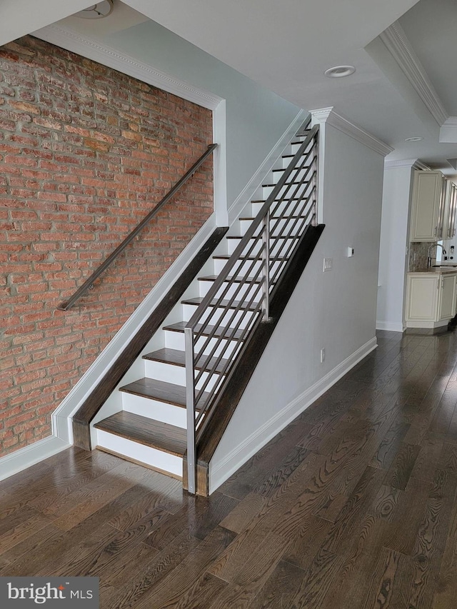 stairs featuring baseboards, crown molding, brick wall, and wood finished floors