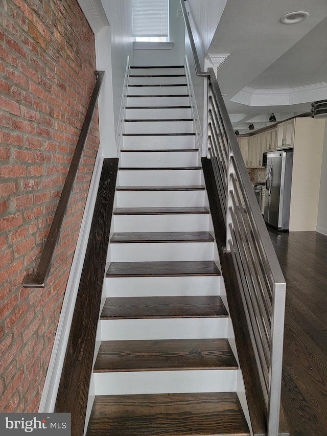 stairway featuring brick wall and wood finished floors