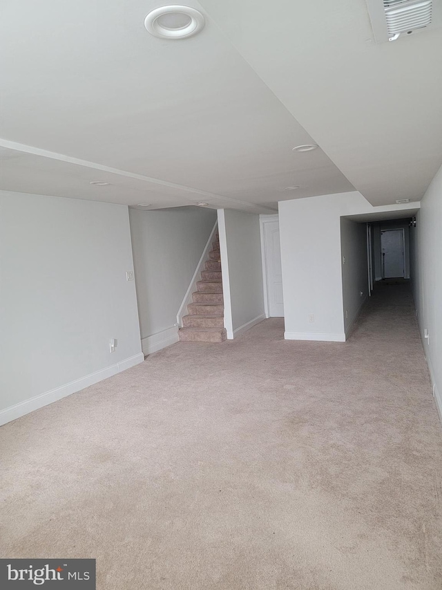 finished below grade area featuring visible vents, light carpet, baseboards, and stairs