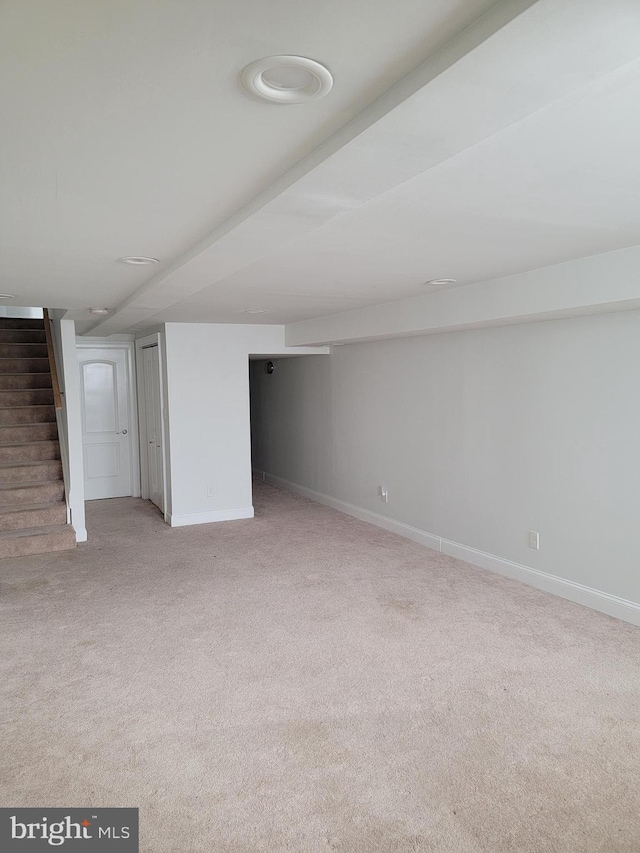 finished below grade area featuring stairs, light carpet, and baseboards