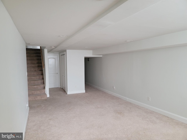 finished below grade area with light colored carpet, stairway, and baseboards