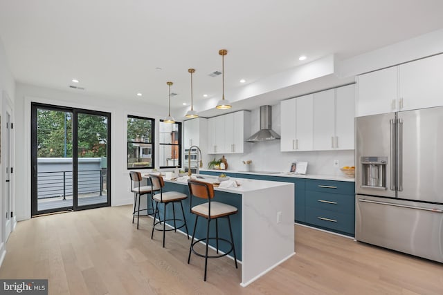 kitchen featuring high quality fridge, a breakfast bar area, a kitchen island with sink, visible vents, and wall chimney exhaust hood