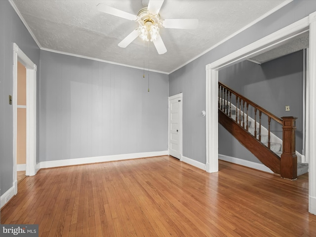 spare room featuring baseboards, a ceiling fan, hardwood / wood-style flooring, stairway, and ornamental molding