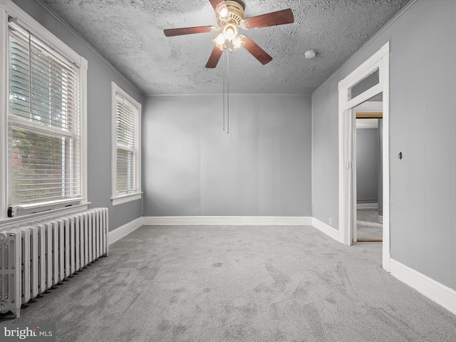 carpeted empty room featuring baseboards, radiator heating unit, ceiling fan, crown molding, and a textured ceiling