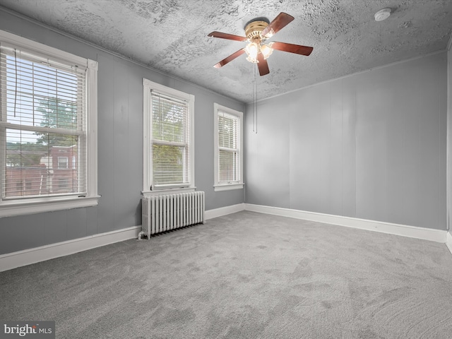 carpeted spare room with a ceiling fan, baseboards, a textured ceiling, and radiator heating unit